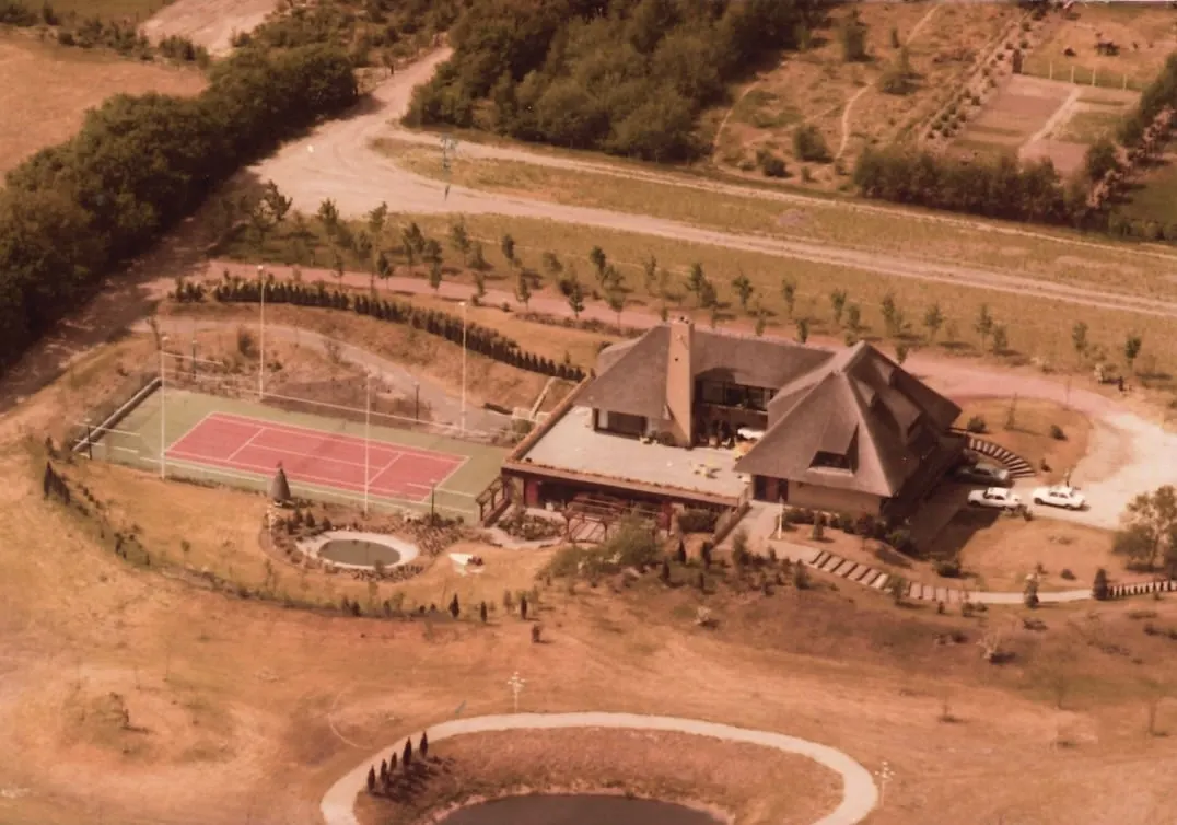 Vista aérea de la dependencia junto al hotel en Nuland, con tejado de paja, pista de tenis y estanque